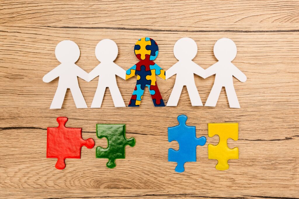 Des silhouettes de papier se tenant par la main, dont une composée de pièces de puzzle, posées sur un plan de travail en bois